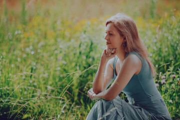 Fototapeta na wymiar Thoughtful elegant young woman sitting in a summer meadow