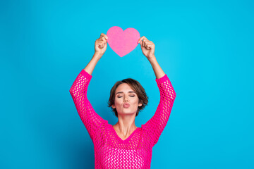 Photo of cheerful flirty woman wear knitted neon shirt sending you kiss rising pink heart postcard...