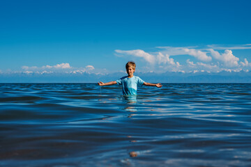 Boy in wet t-shirt stands in the lake and enjoys good weather