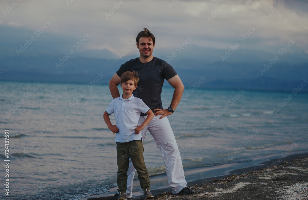 Wall mural Happy father and son standing on lake shore at windy weather