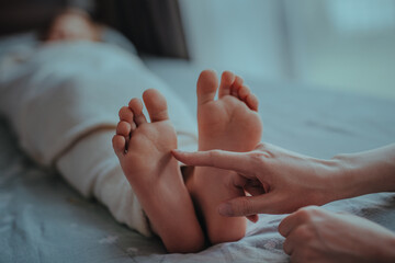Woman's hand touches foot of sleeping child - obrazy, fototapety, plakaty