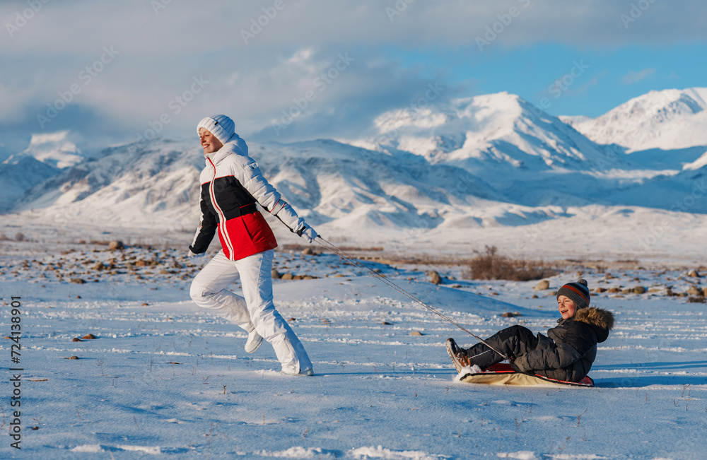 Canvas Prints Happy young woman sledding her son in winter on mountains background