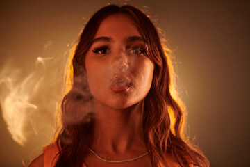 Portrait of young woman breathing out smoke and looking at camera