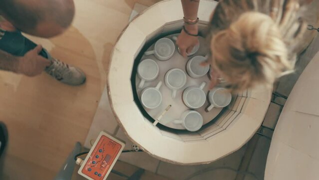 Electric kiln, cup and pottery people put ceramic in oven for creative workshop, manufacturing process or design. Clay. mug, top view and artist teamwork on art product with heating machine