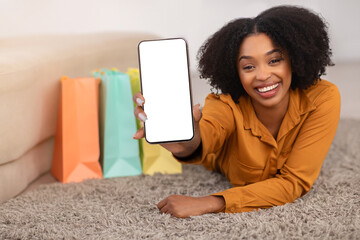 Glad millennial african american curly lady with bags show smartphone with empty screen