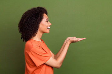 Photo of positive cute lady dressed orange t-shirt holding arms empty space smiling isolated khaki color background