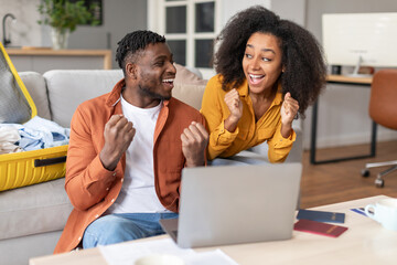 african spouses gesturing yes near laptop celebrating upcoming vacation indoors