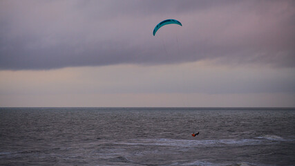 Kitesurfing. Kiteserferzy o zachodzie słońca na tle złocistego morza. Silny wiatr tworzy doskonałe warunki do powietrznych ewolucji. Pastelowe kolory, low key.
