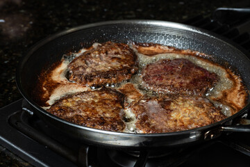Frying schnitzel in a pan on gas cook top. Home cooking concept.