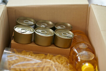 Box with canned food, vegetable oil and macaroni packed for family in need - obrazy, fototapety, plakaty