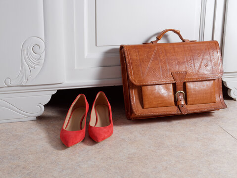 Cartable en cuir et chaussures de femme devant un meuble