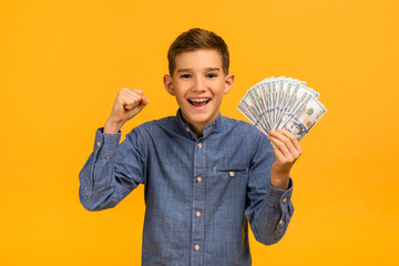 Joyful teen boy triumphantly raising fist while holding dollar cash