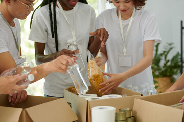 Charity organization workers putting packages of macaroni and bottled water in cardboard boxes