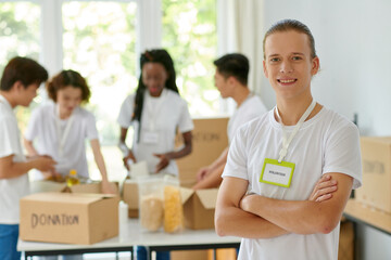 Portrait of smiling volunteer of charity organization, his friend packing donated products in...