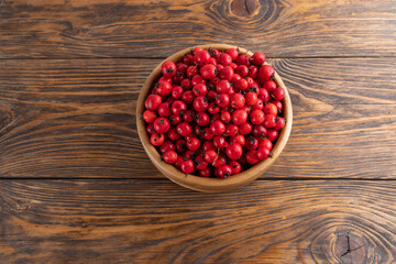 red hawthorn berries in wooden bowl on flat wooden surface.