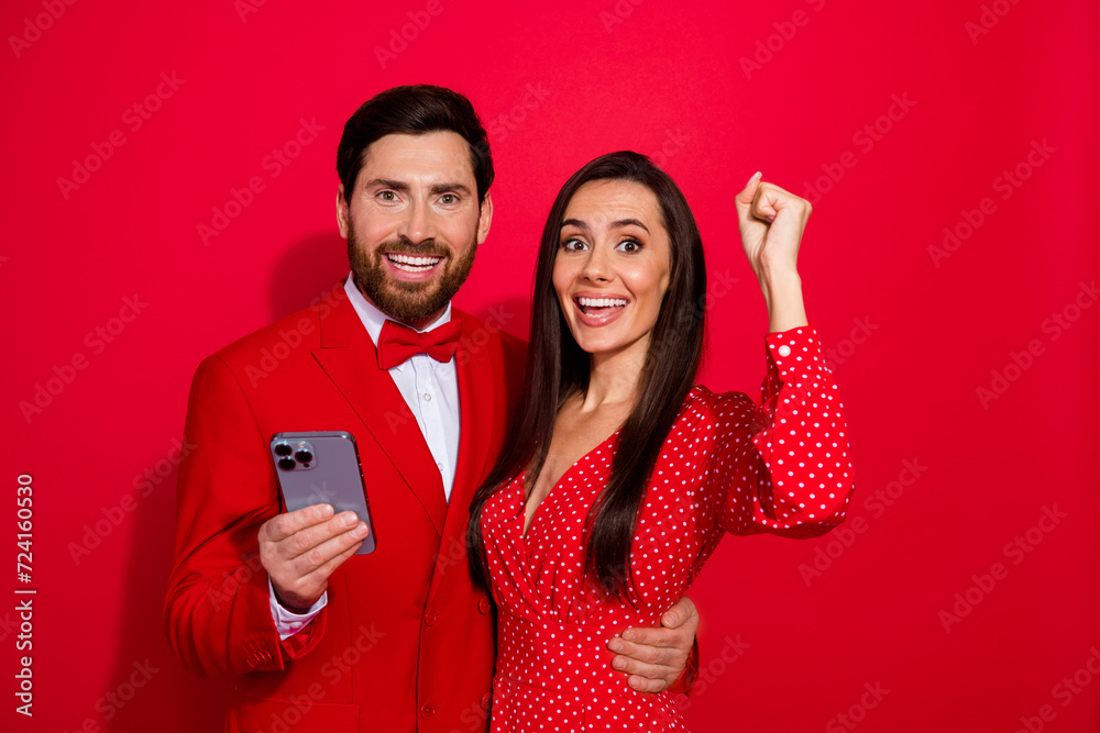 Poster photo of two attractive delighted lovers embrace hold smart phone raise fist empty space isolated on