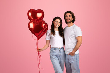 Content couple standing close, with the woman holding shiny red heart-shaped balloons