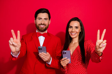 Photo of two friendly positive people hold smart phone demonstrate v-sign isolated on red color background