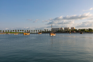 Obraz premium A view of the garden of the Museum of Islamic Art in Qatar, with the sea, boats and palm trees, with Doha Towers 