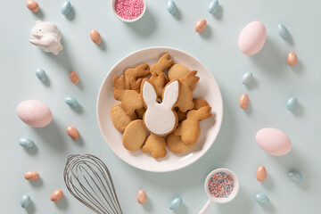 Easter homemade glazed bunnies shaped cookies, pink eggs in white plate on blue background....