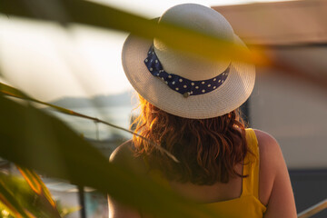 Female stands on the shore and looks out to sea. Palm leaves in the foreground 