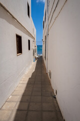Fototapeta na wymiar Seascape. Alley facing the sea. Fishing village of Arrieta. Houses with white walls and blue windows. Lanzarote architecture. Lanzarote, Canary Islands, Spain