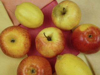 Fresh ripe yellow red apples and yellow lemons lying on the multi-colored fabric napkins in the colors of the fruits lying on them, background