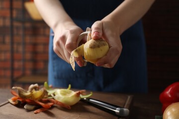 Woman peeling fresh potato at table indoors, closeup - obrazy, fototapety, plakaty