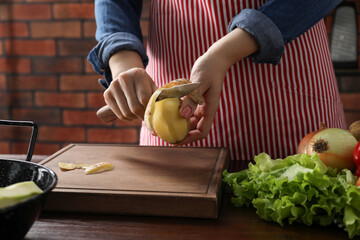 Woman peeling fresh potato with knife at wooden table indoors, closeup