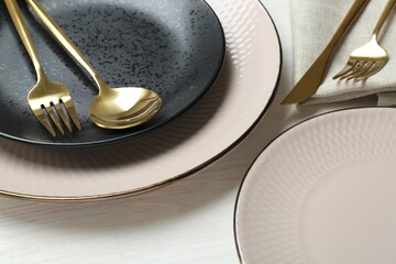 Stylish ceramic plates and cutlery on white wooden table, closeup