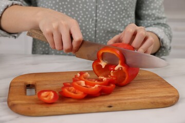 Cooking process. Woman cutting bell pepper at white countertop, closeup