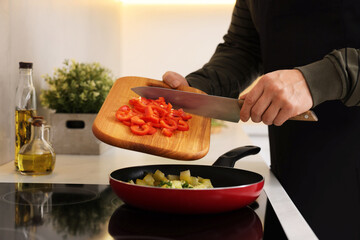 Cooking process. Man adding cut bell pepper into frying pan in kitchen, closeup