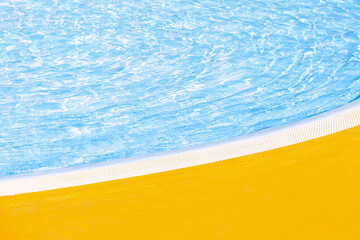 Outdoor swimming pool edge with curved border in sunny summer day. Clear blue water and yellow...