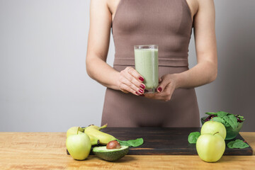 Unrecognizable athletic woman in sportswear holding glass of healthy green vegan smoothie. banana,...