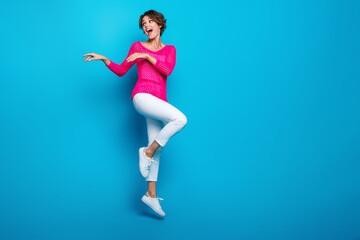 Full length photo of funky carefree woman wear knitted neon shirt jumping high dancing empty space...