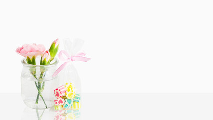 Delicate pink flowers in a small vase. Sweet lollipops and candies in a bag. On a light background with empty space