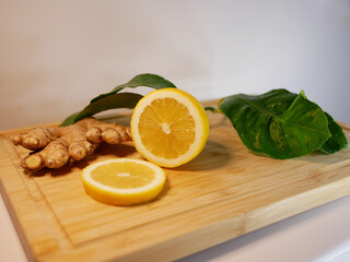 Cut lemon with green leaves and ginger on a wooden board