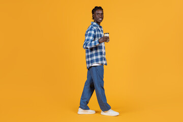 Fototapeta na wymiar Relaxed young black man walking with takeaway coffee cup in hand
