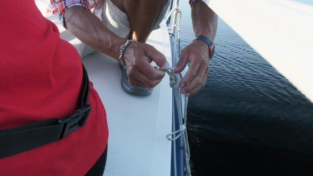 Seasoned yachtsman ties mooring ball to deck with nylon rope. Sailor prepares docking equipment for safe stay in open waters