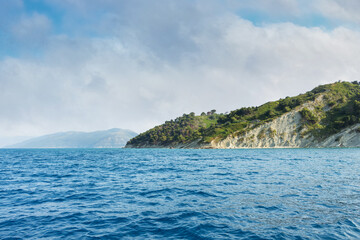 Obraz premium The sea with a rocky shore on the background of a blue sky with white clouds