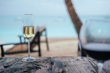 A glass of sparkling wine on a wooden table. Exotic island - palms, blue sea, sand 