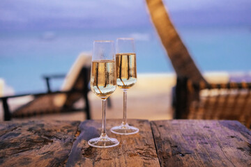Two glasses of champagne in an outdoor cafe on an island, palm trees, sea, sunset 