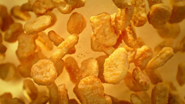 Super Slow Motion Shot of Flying Chicken Nuggets Towards Camera on Golden Background at 1000fps.