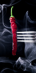 Smoke on a black background, with red chili pepper on a fork. Close-up, vertical.