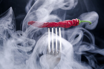 Dried red chili peppers on a fork with smoke on a black background.