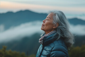 A senior woman doing breathing exercise in nature on early morning with background of mountains - obrazy, fototapety, plakaty