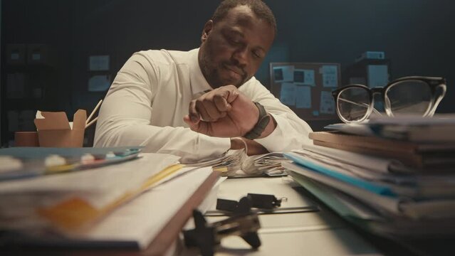 Stab shot of exhausted Black businessman sleeping at office desk with stacks of documents in folders on it, working overtime at night meeting deadlines