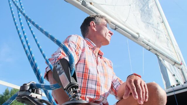 Relaxed man in sunglasses sits on deck talking to crew. Avid yachtsmen enjoy sailboat ride on sunny day. Perfect weather for yachting