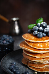 Pile of pancakes with blueberries on a plate on a dark background  - obrazy, fototapety, plakaty