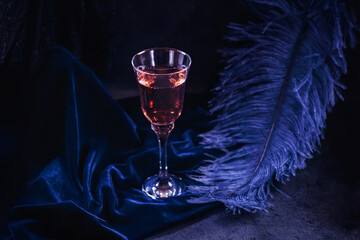 Glass of rose sparkling wine and large blue feather on dark blue velour background. Beautiful...